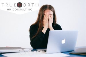 Woman hides face in frustration while using laptop.