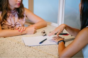 Two women brainstorming ideas at a table with pen and paper.