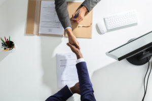Two individuals shaking hands across a desk.