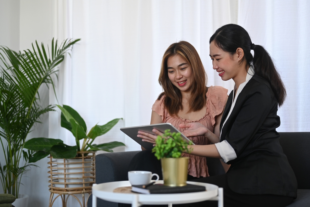 Two business women on a couch, focused on a tablet.