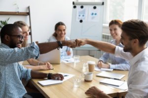 A business meeting with people fist bumping at a table.