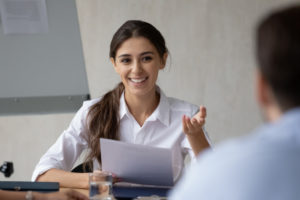 A happy businesswoman holding a document while talking to a man at a desk.