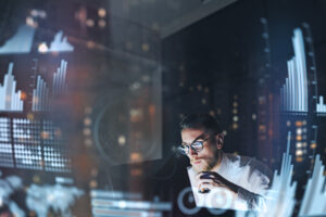 A man in glasses analyzing graphs on a screen.