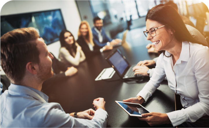 Two colleagues discussing work on a tablet during a team meeting at a table.
